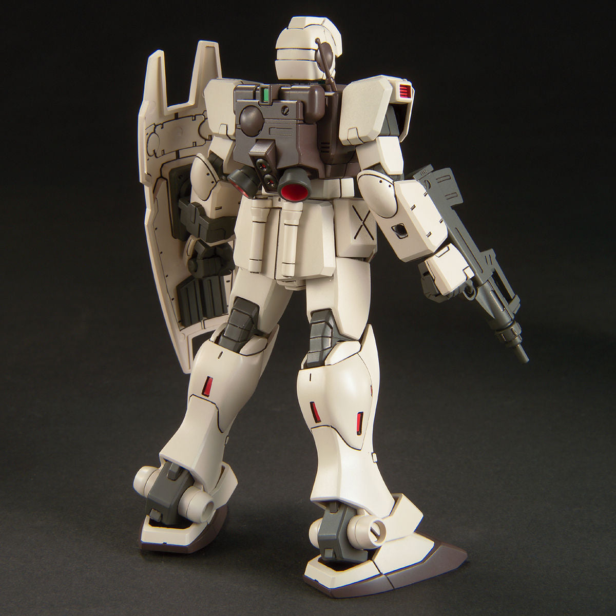 Off-white Gundam model kit viewed from behind, featuring a backpack, shield, and rifle on a black background.