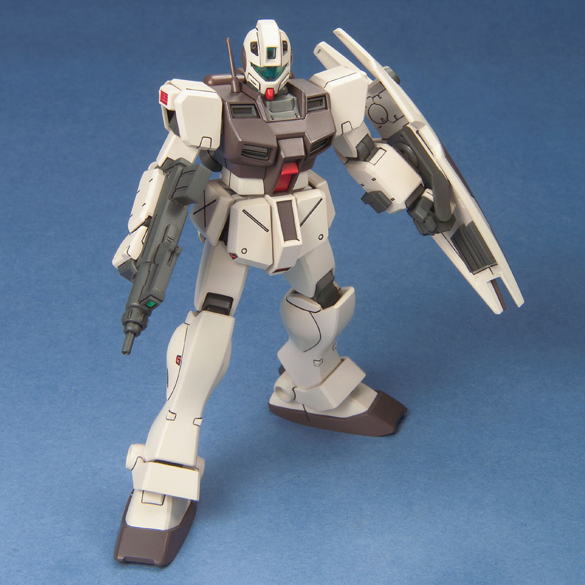 Off-white and gray Gundam plastic model kit with a rifle and shield, standing in a dynamic pose on a blue background.