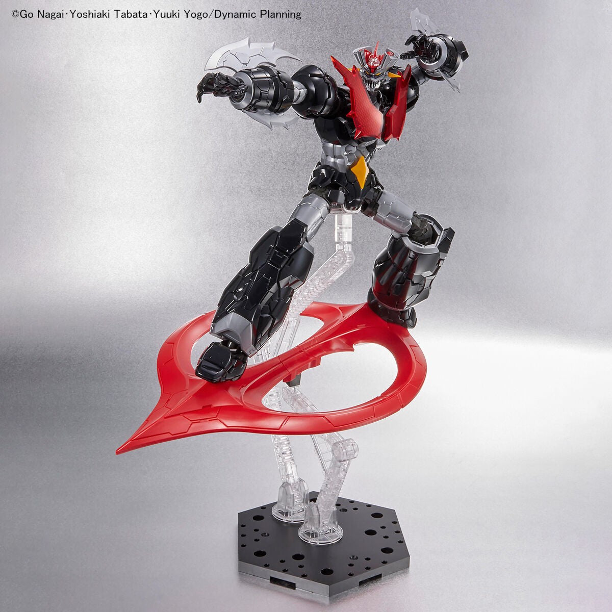 Mazinger Z action figure in black, silver, and red, posing dynamically on a stand with a large red wing-like accessory.