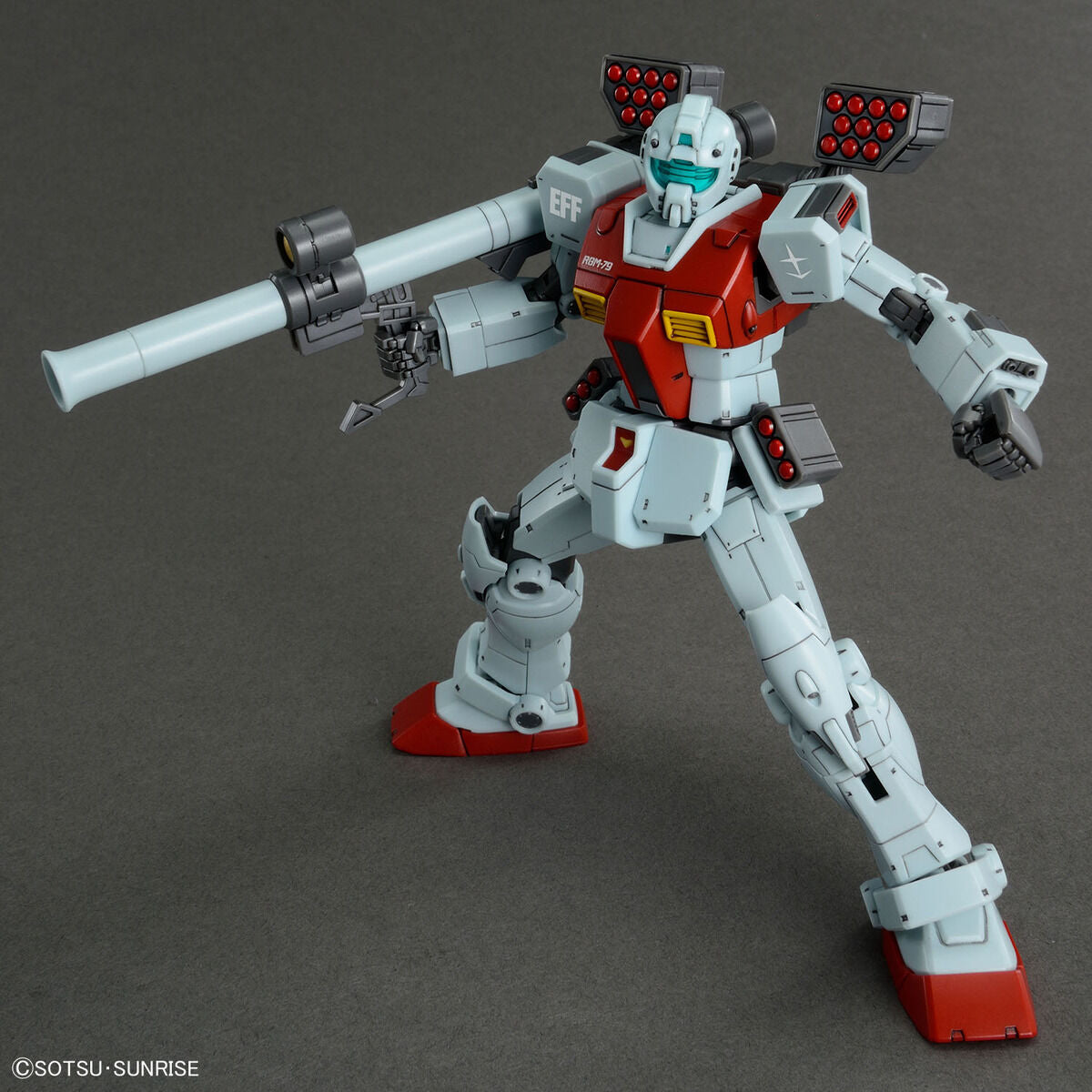 Model kit Bandai HG 1/144 GM con cannone a spalla e pod missilistici, robot in posa da combattimento.