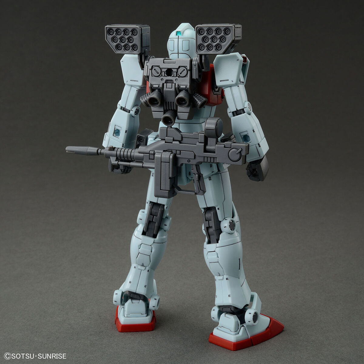 Vista posteriore del model kit Bandai GM HG 1/144 con missile pod e fucile, su sfondo grigio.