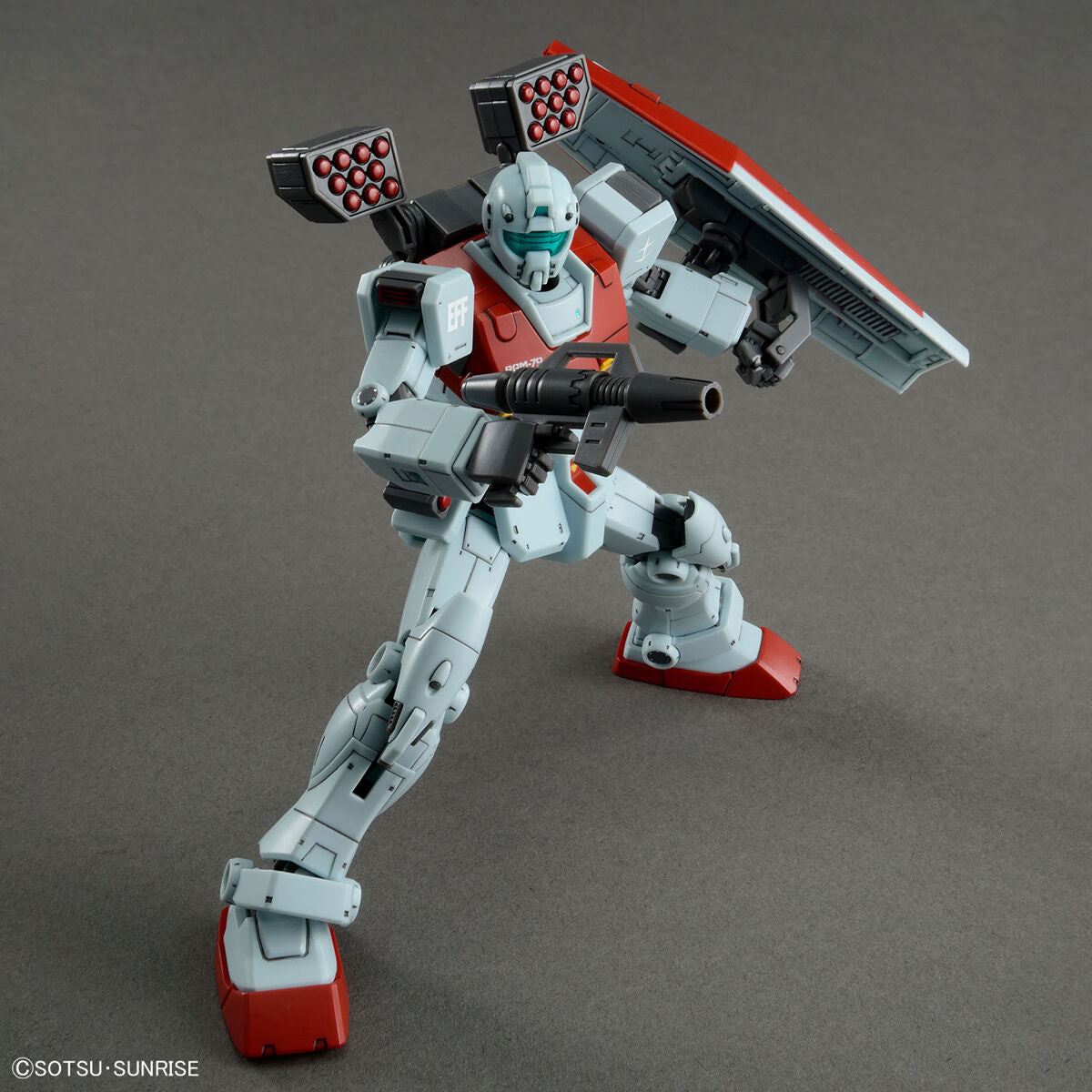 Model kit Bandai HG 1/144 GM con cannoni a spalla, missile pod e scudo. Robot assemblato in posa dinamica.