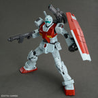 Model kit Bandai HG 1/144 GM con cannone a spalla, scudo e fucile, in posa dinamica su sfondo grigio.