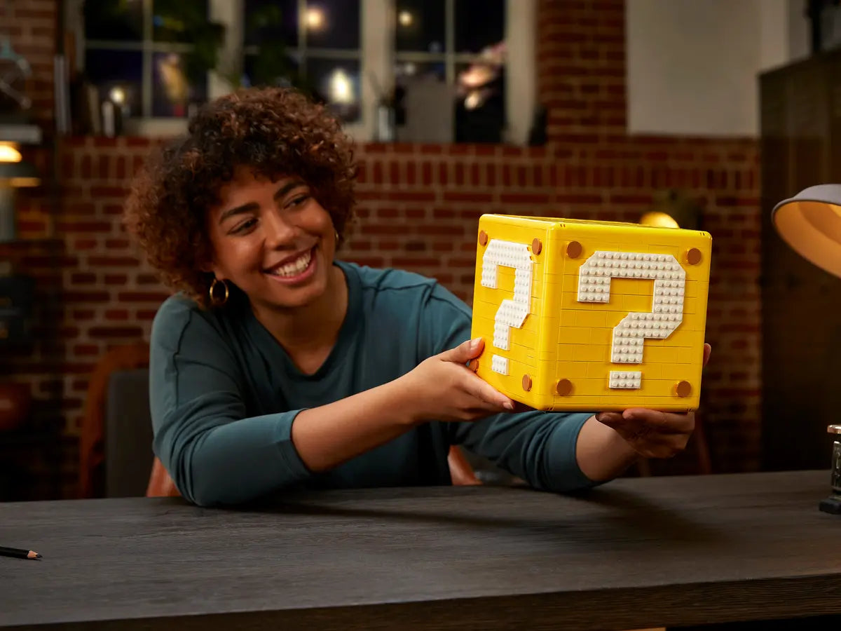 Donna sorridente tiene in mano il set LEGO Super Mario 71395 Blocco Punto Interrogativo su un tavolo in ufficio.