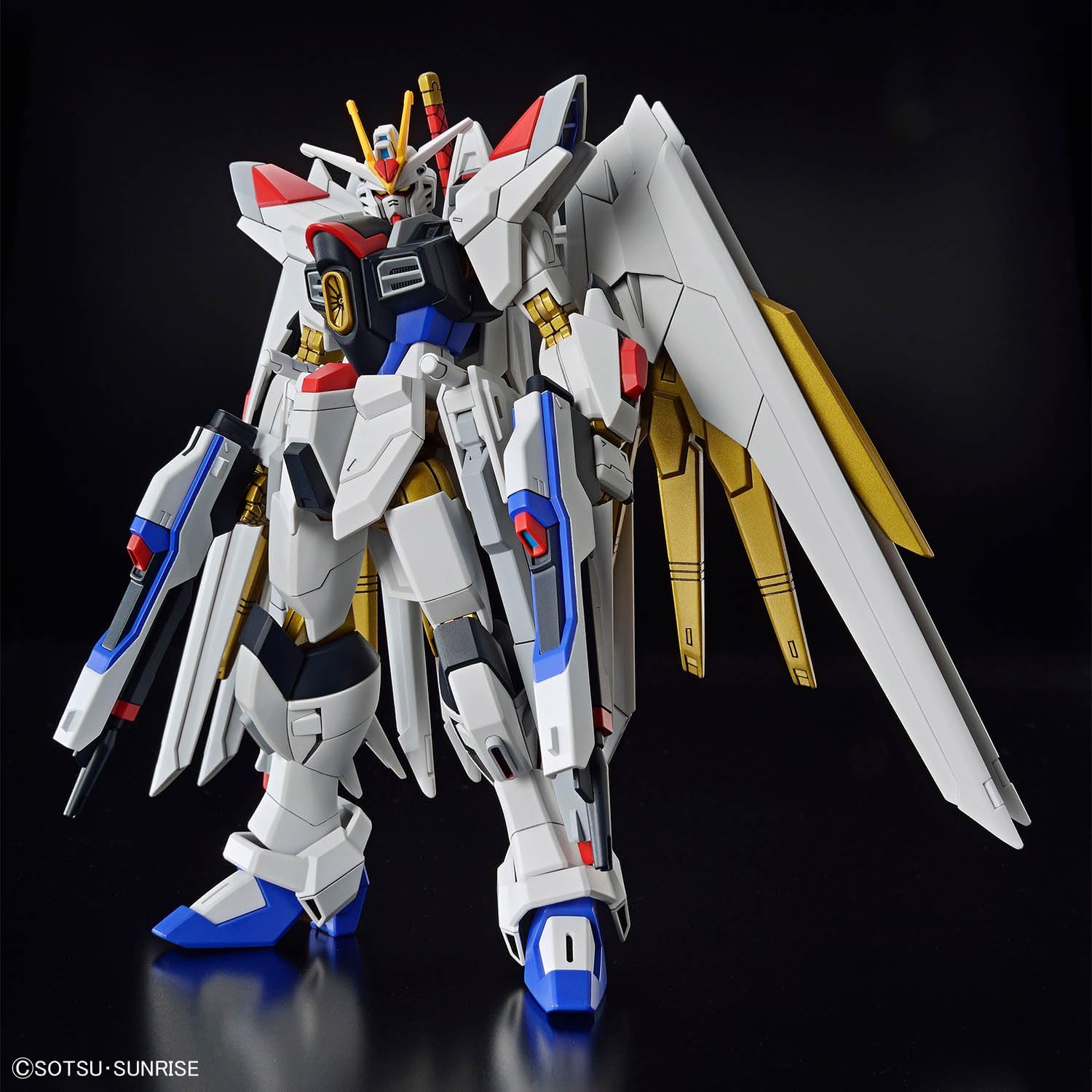 Model kit Bandai 1/144 HG Mighty Strike Freedom Gundam: robot bianco, blu e oro su sfondo nero.