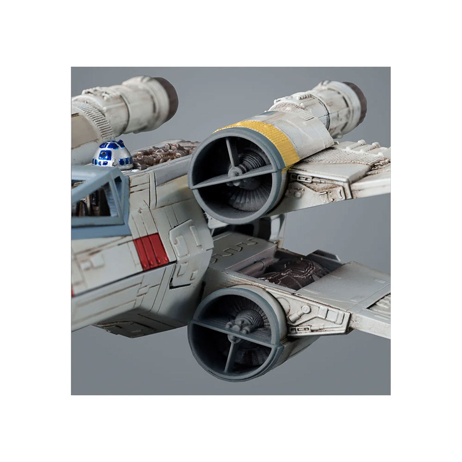 Detailed model of a Star Wars X-wing fighter, white with red markings, featuring an R2-D2 droid and weathered finish.